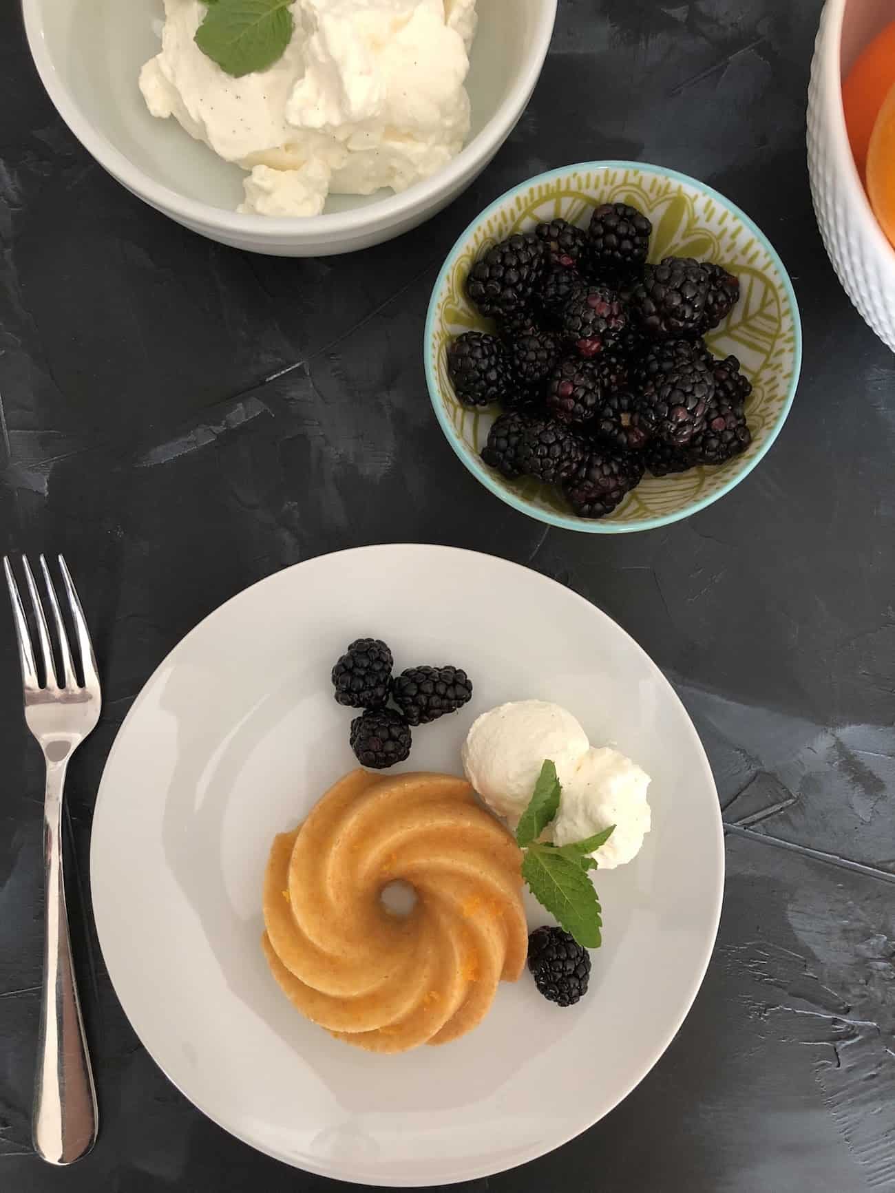 orange bundlette with bowl of whipped cream, blackberries, and bowl of oranges