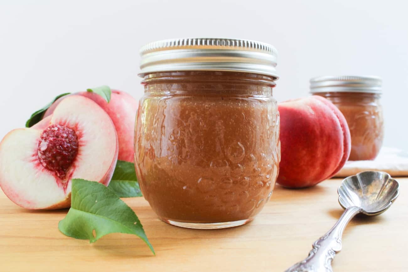 peach butter in jar with peaches and spoon